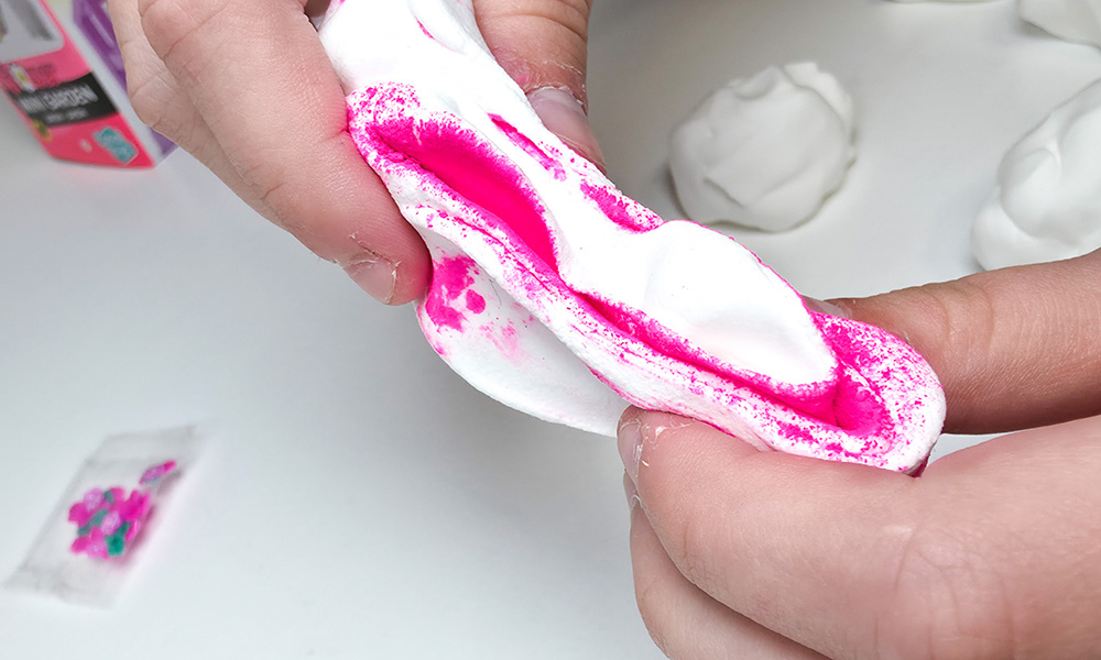 child mixing bright pink powder into white so slime butter slime