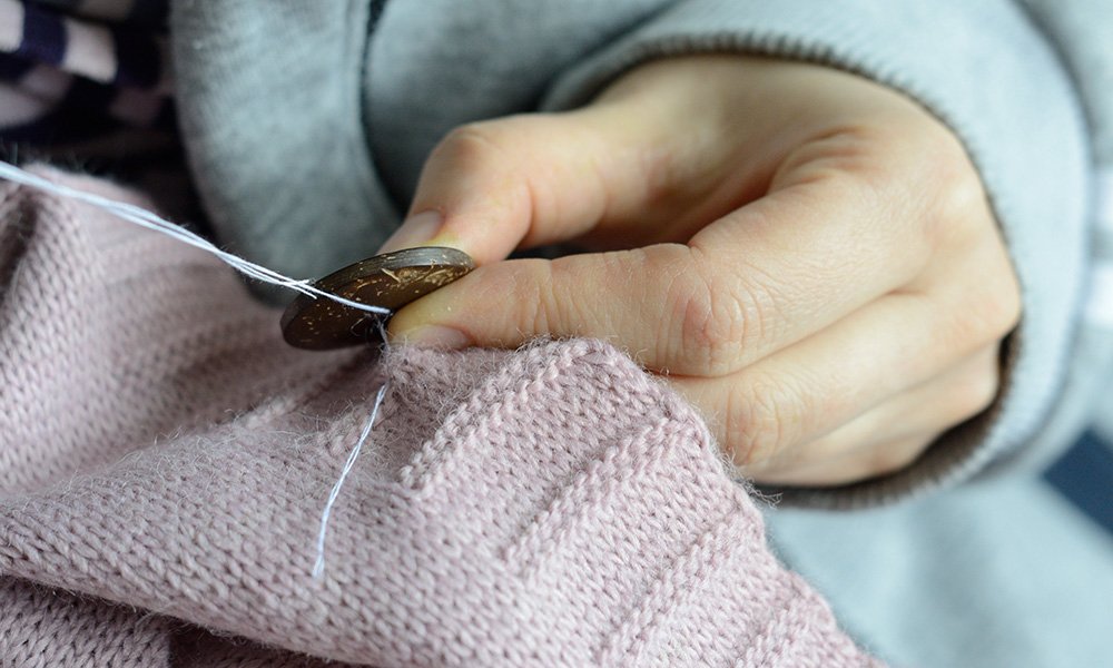 female workers' hands sew a wooden button to a jacket. close-up.